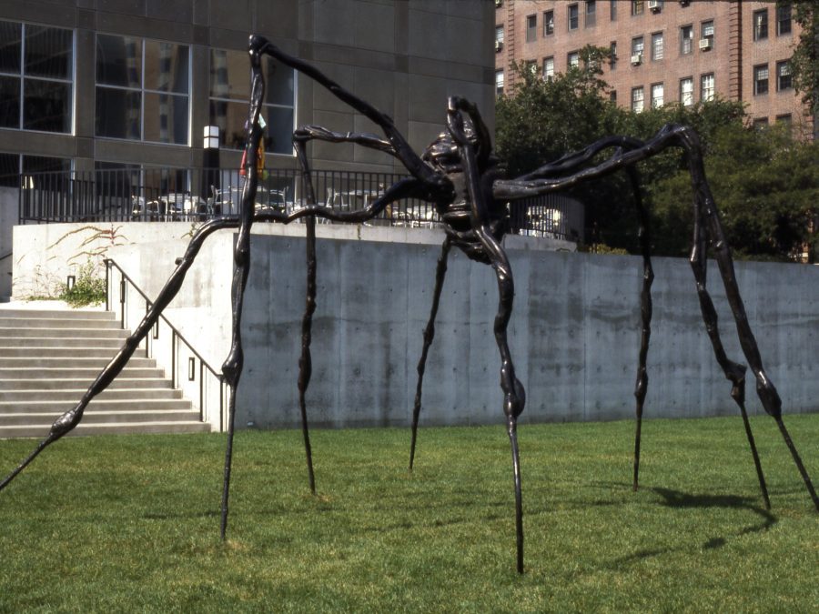 A larger black sculpture resembling a giant spider in the middle of a park with steps and a concrete wall behind it
