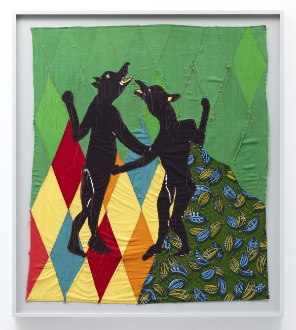 Two black figures with human bodies and dog heads appear on a patterned background of green, red, yellow, orange, and blue diamonds and section of green, light green, and blue-printed fabric.