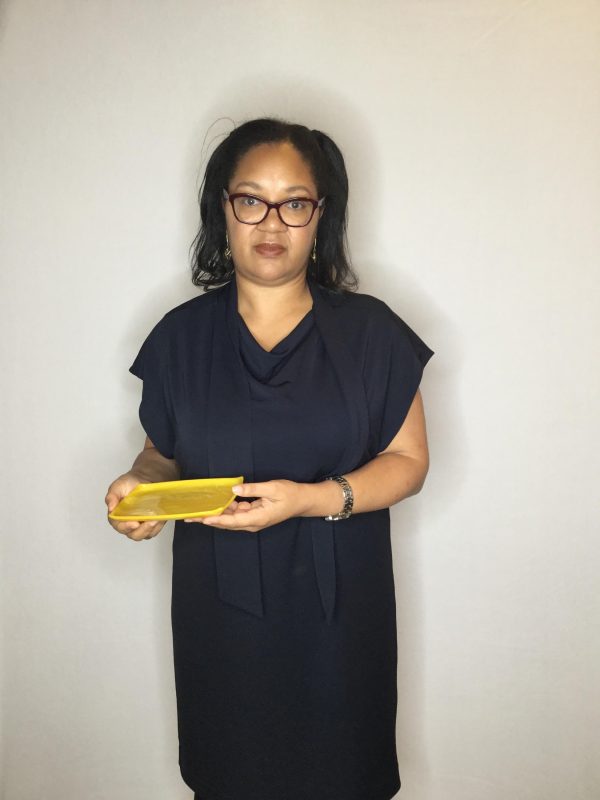 A female presenting person with medium length black hair and glasses holds an object with both hands against her right side