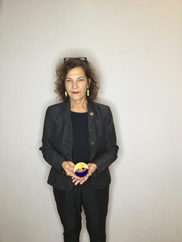 A female-presenting person with medium length curly brown hair holding a small object in both of their hands at their waist
