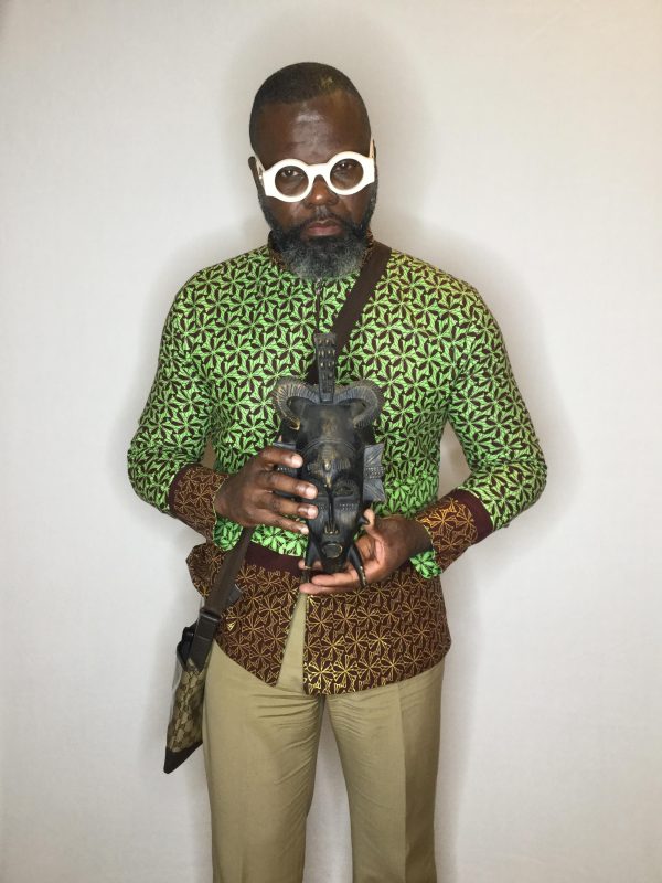 A male-presenting person with eye-catching white glasses holds a sculpture in both hands