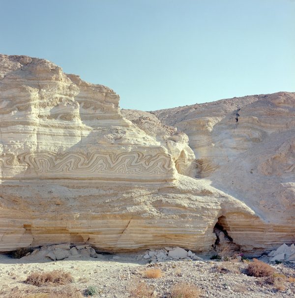 A barren, mountainous desert setting with wavy patterns in the rock breaking up the linear strata