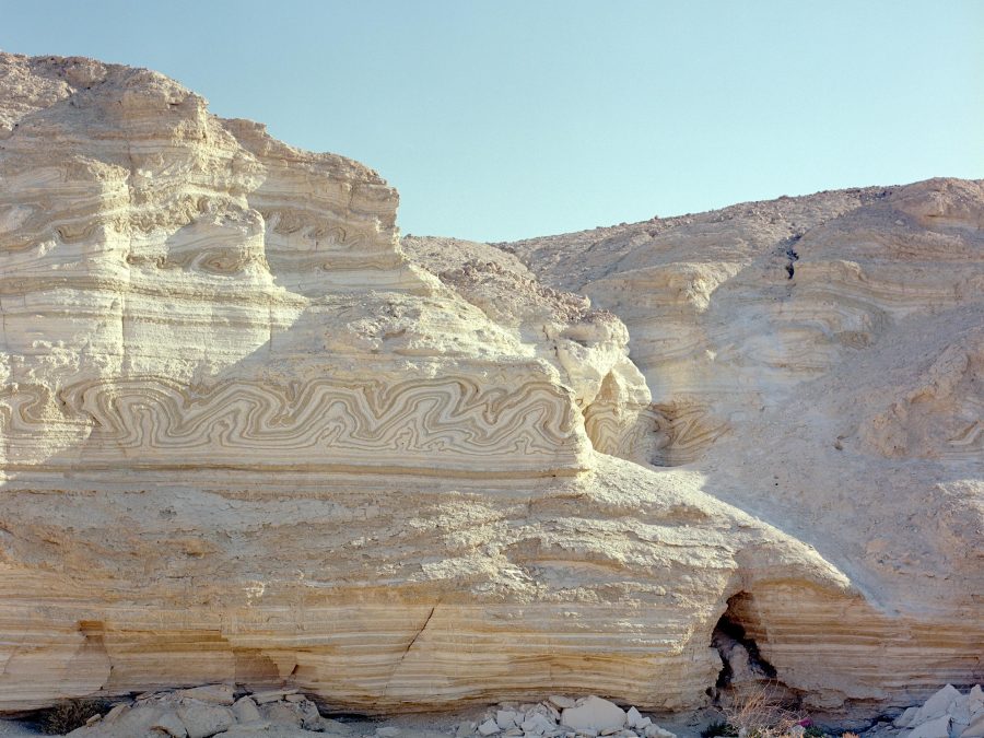A barren, mountainous desert setting with wavy patterns in the rock breaking up the linear strata