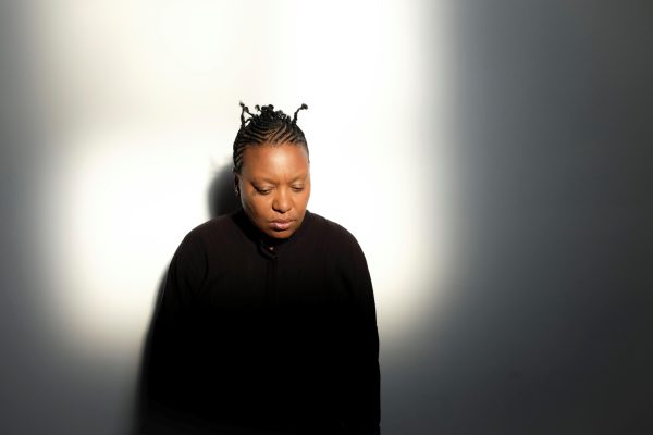 Portrait of a person with short black hair dressed in black lit by a bright square of light