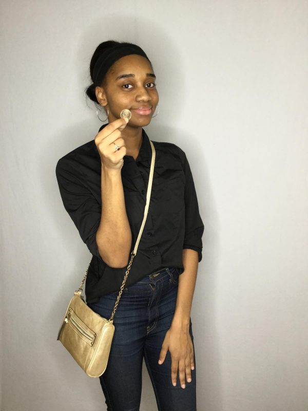 A female-presenting person with medium-dark skin holds a tiny object up in their right hand with two fingers