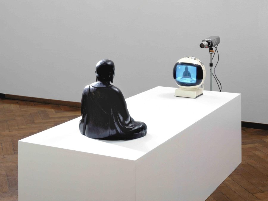 A statue on a white pedestal in front of a tv and camera displaying a live feed of the statue