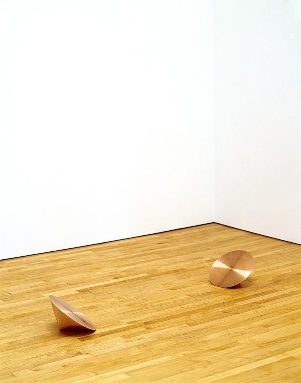 Two copper cones on a wooden floor placed so their flat sides are facing up