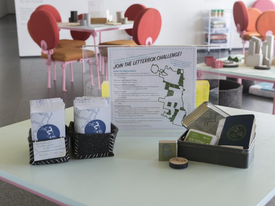 A table with an instruction sign, stamps, and paper on in in a room filled with orange chairs around tables