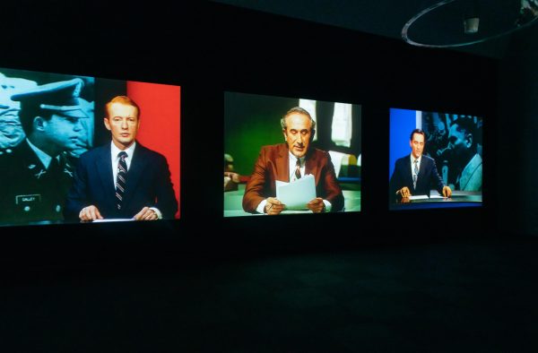 Three screens in a dark room featuring three different news anchors from various decades