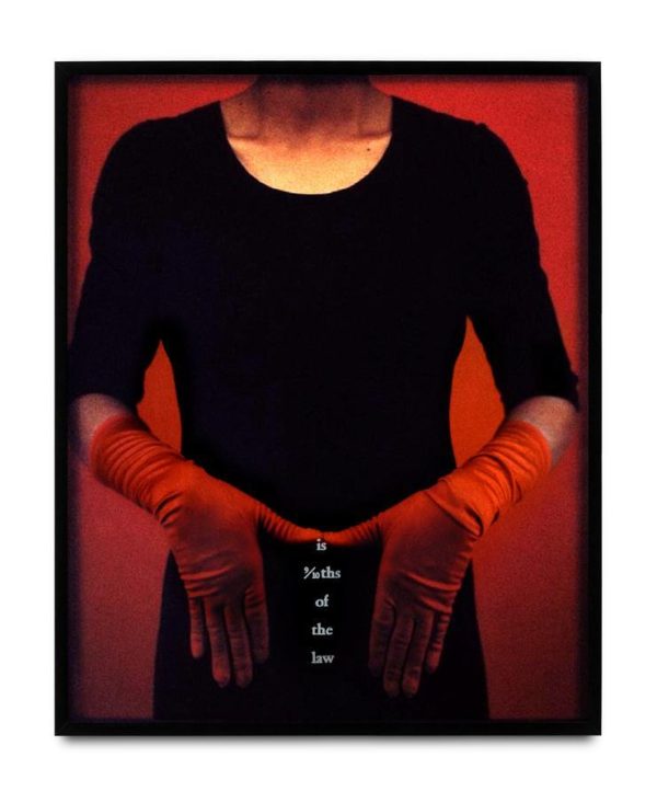 The torso of a person dressed in black with red satin gloves on, hands placed in an m-shape at their hips