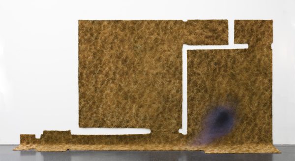A scrap of fabric with portions cut out of it hangs on the wall and spills onto the floor