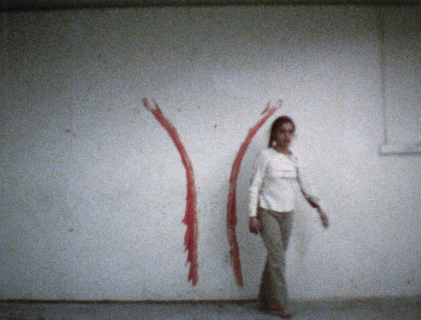 A person walks away from a white wall with two red lines that curve in to run parallel at their lower halves
