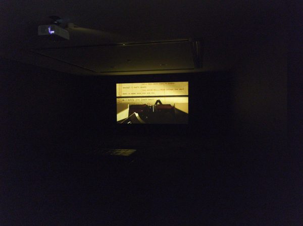 Video projected onto the wall of a dark room featuring a close up of a typewriter key on yellow paper