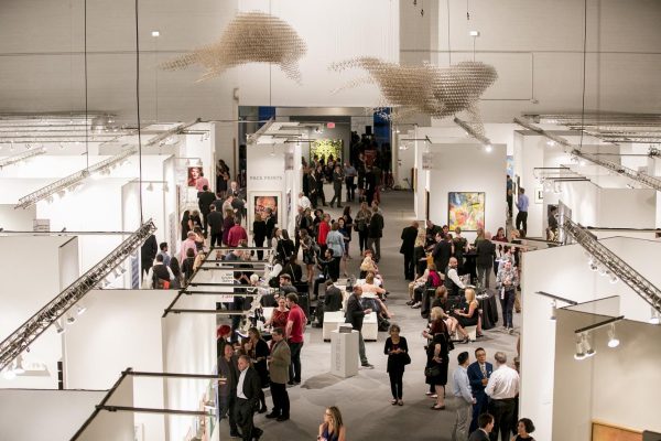 Two sculptures hover above a large space filled with white room dividers and people.
