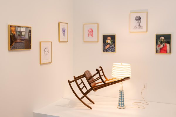 Artworks in a gallery lit by a warm glow. A rocking chair appears to float in midair in front of several framed works of art hanging on the wall.