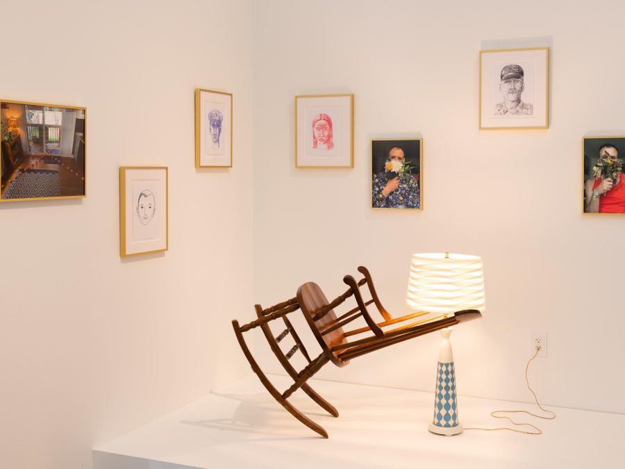 Artworks in a gallery lit by a warm glow. A rocking chair appears to float in midair in front of several framed works of art hanging on the wall.