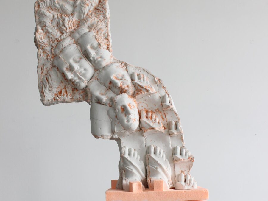 A wave-like sculpture made up of repeating heads and feet on a white pedestal in a gallery space