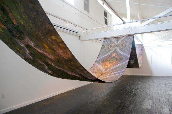 A long sheet of fabric is strung up in waves in a white gallery space