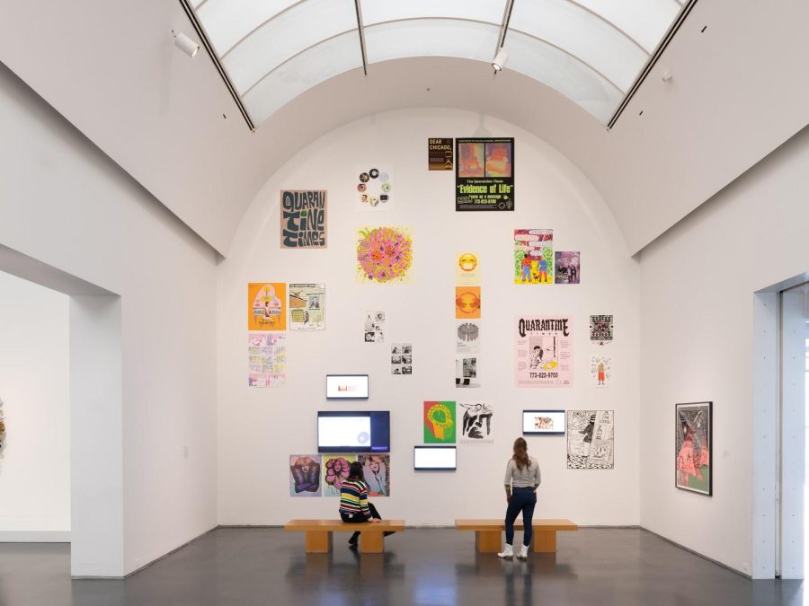 Two people view artworks displayed all over a tall arched white wall in a gallery space