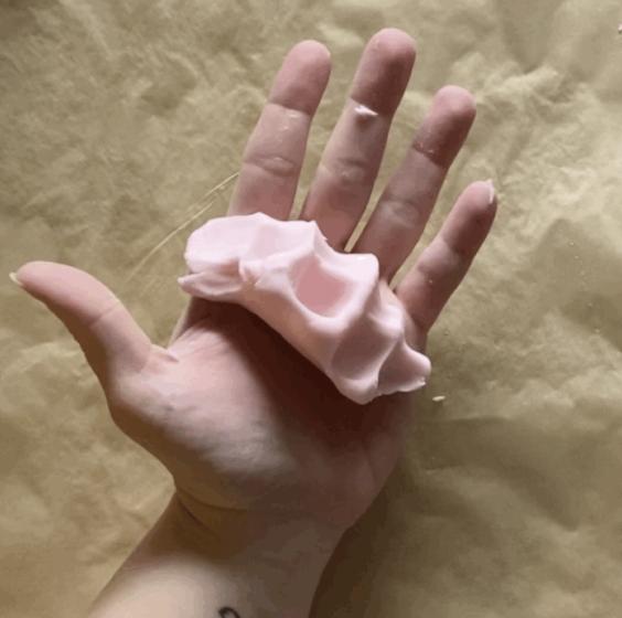 A left hand holds out a pink object that has the imprints of the fingers in it from being squeezed
