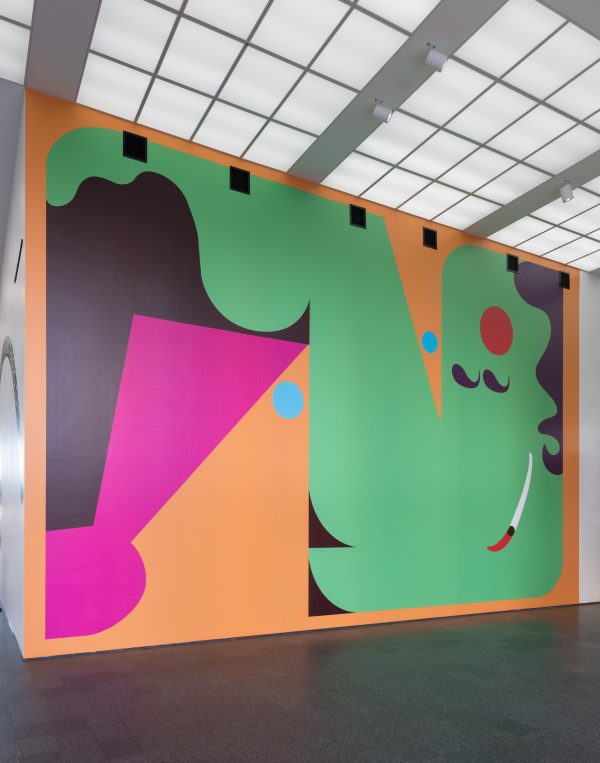 A colorful, abstract mural consisting mostly of green, pink, and black shapes on an orange background slightly resembling a reclining person with a mustache