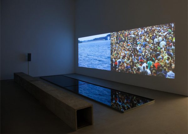 Two images are projected side by side on a wall in a darkened room. On the floor is a dark rectangle that reflects the images on the screen