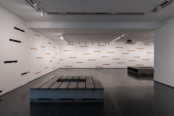 Gallery view with two pallets on the floor and walls with many long, rectangular cut-outs.