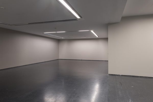 An empty gallery space with el-shaped neon lights reflecting on the floor from the ceiling