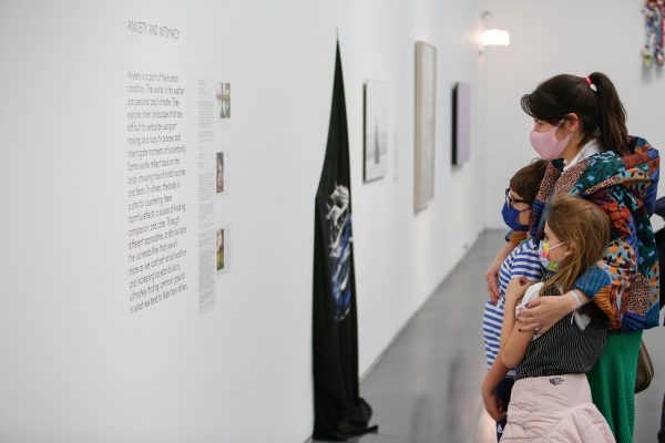 And adult hugs two children while looking at art. All three are wearing masks.