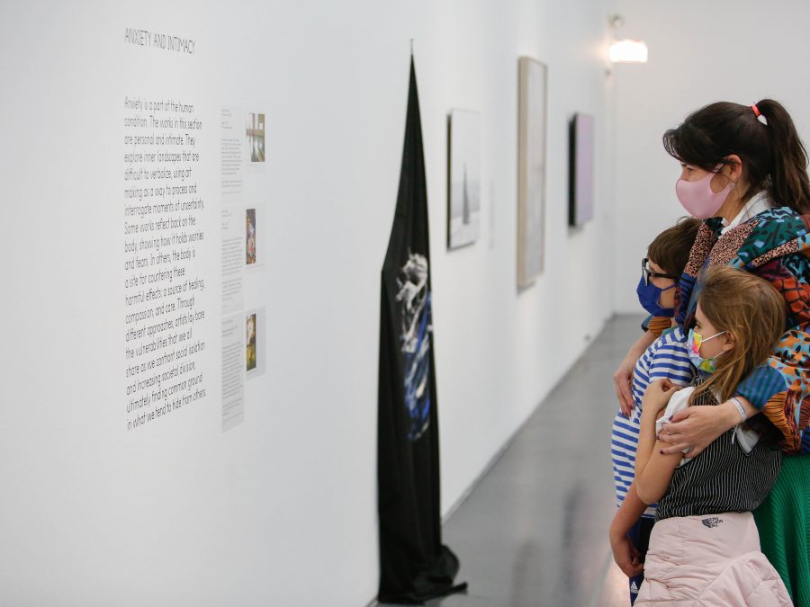 And adult hugs two children while looking at art. All three are wearing masks.