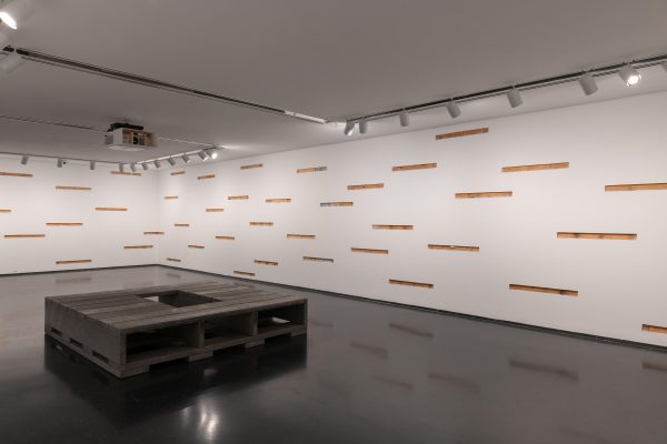 A gallery with many horizontal cutouts of the wall revealing the structure behind it. In the middle of the room is a square grey pallet