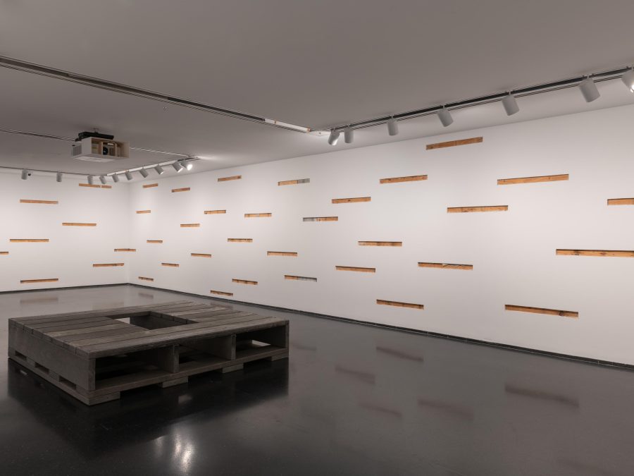 A gallery with many horizontal cutouts of the wall revealing the structure behind it. In the middle of the room is a square grey pallet