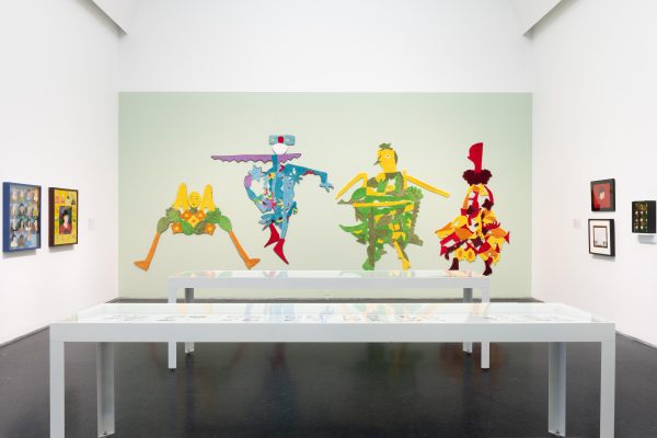 Exhibition interior with figurative illustrations on far wall and tables in the foreground
