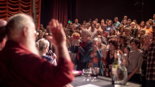 An audience raises their right hand while they watch a performance