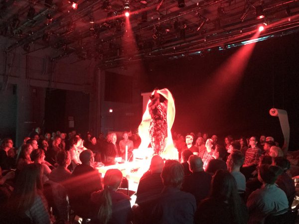 A person stands on a stage in the center of an audience