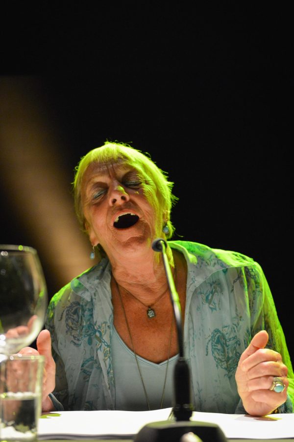 A woman is seated under a soft green light with her eyes closed and mouth open