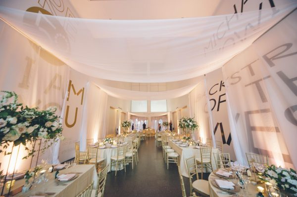 Tables set for wedding reception under a sheer curtain canopy in a multistory room