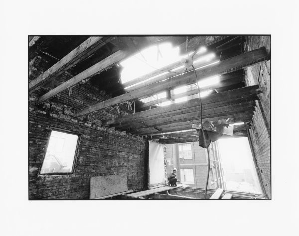 View from inside a building. A person sits at the edge of the front of the building where a wall should be.