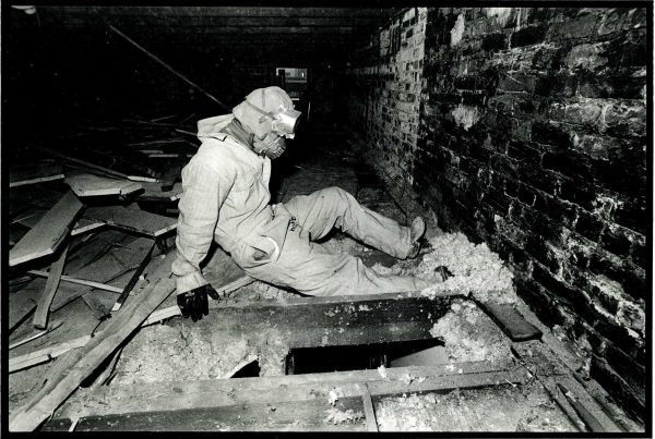 A person wearing a mask and coveralls kicks at material next to a hole in a floor.