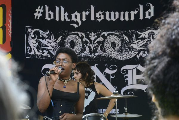 View from the crowd of a singer holding a microphone. A drummer is just visible behind them.