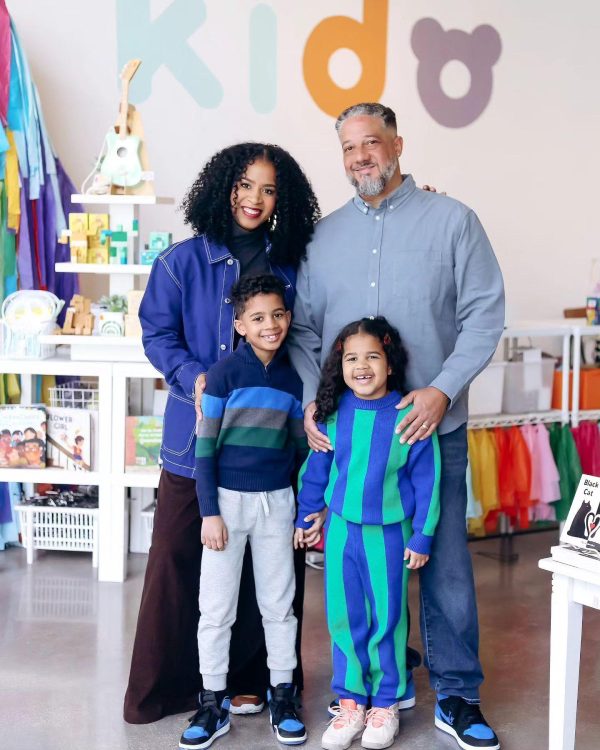 Two adults and two children pose in a store. A variety of toys and clothing is on display and the word kido appears on the wall behind them.