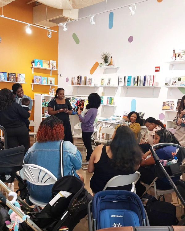 A group of people and strollers gather in a circle in a colorful store filled with books.