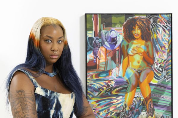 A Black female-presenting person with striking hair poses in front of a painting of a half-naked woman covering her breasts.